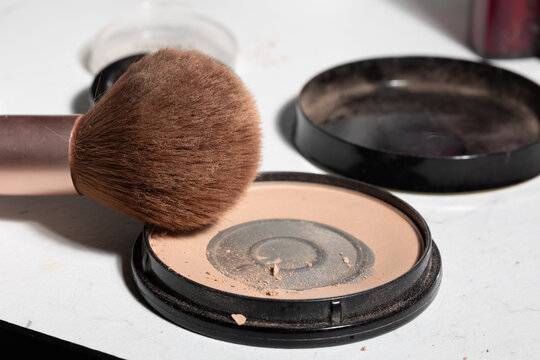 Close-up of a worn makeup brush resting on an open beige compact with powder dust and residue, conveying authentic, unpolished use while highlighting shelf-life, hygiene, and daily routines.