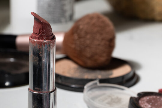 Close-up of a partially used mauve lipstick in a silver case on a vanity, showing a cracked tip, smeared exterior, and visible residue to convey real makeup wear, hygiene cues, and shelf life.