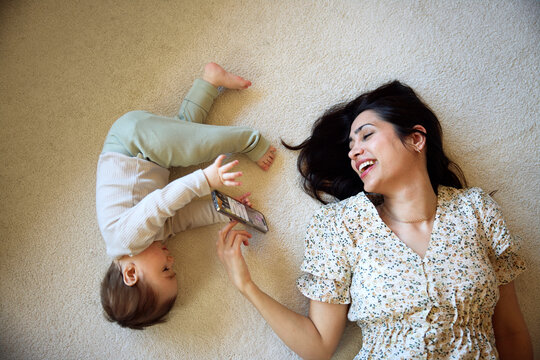 High angle view of happy mother playing with baby boy while lying on carpet at home