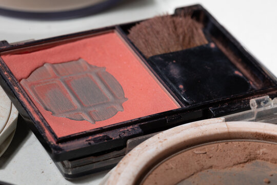 Macro close-up of a partially used pink coral blush palette, powder dust and a worn brush suggestive of real-use hygiene, shelf-life cues, and need for replacement in everyday makeup routines.