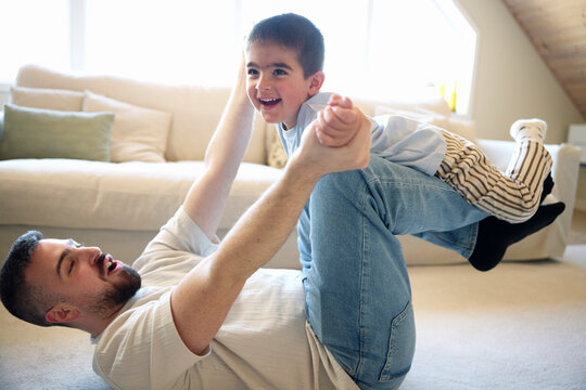 Carefree man picking up son on legs while playing in living room at home