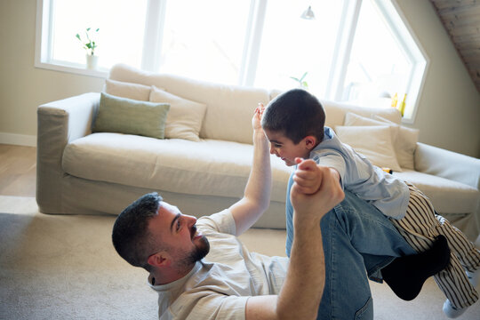Carefree man lifting his son on legs while enjoying leisure time at home
