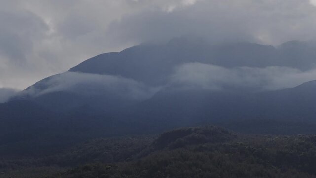 Cloud and fog on rugged mountain peak with forested foothills
