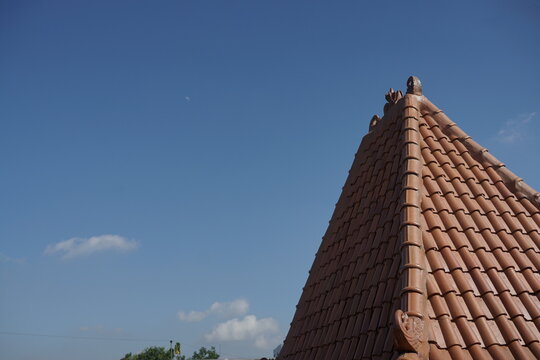 Terracotta tile roof corner against a clear azure sky, showcasing traditional architecture and a serene outdoor atmosphere, with subtle clouds hinting at a bright day