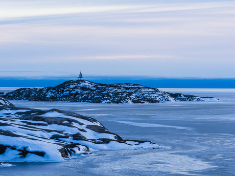 Tranquil view of winter coastal landscape with snow covered rocky slope near frozen sea water at dusk