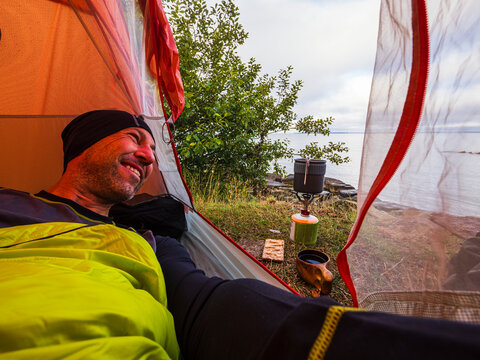Smiling man lying in tent while camping near river