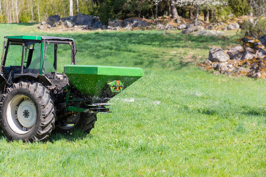 Tractor with rear mounted fertilizer spreader dispersing water across grassy field
