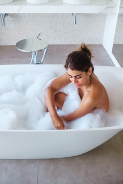 A white woman relaxes in a bubble bath in a modern bathroom