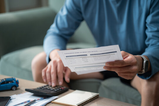 Male hands holding bank payment due notice paper while using calculator to review financial document and calculate monthly bill expense at desk