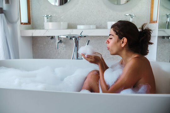 A white woman enjoys a relaxing bubble bath in a modern bathroom