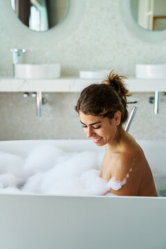 A white woman smiling and relaxing in a bathtub with bubbles