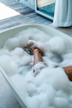A white person relaxing with legs in a bubble bath inside a bathtub