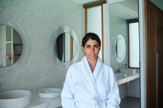 A woman wearing a white bathrobe stands in a modern bathroom