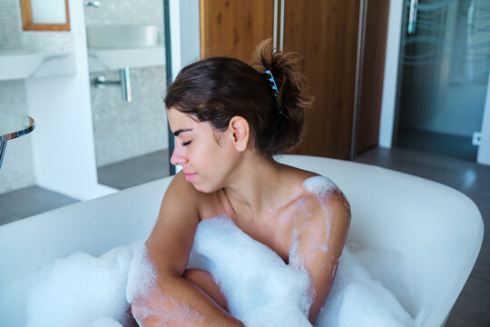 A white woman relaxing in a bubble bath in a modern bathroom
