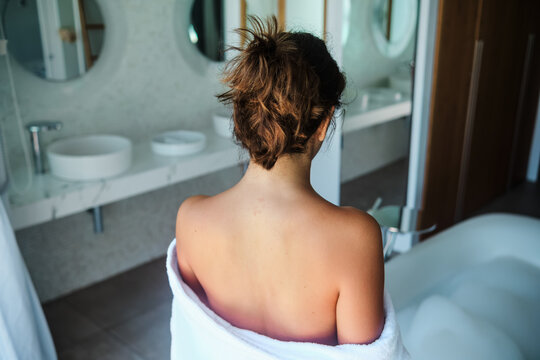 A white woman wrapped in towel relaxing by a foam bathtub