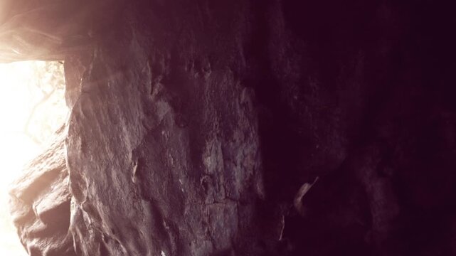 Light enters through a narrow opening in a rock formation inside a cave. Shadows create a contrast with the bright areas, highlighting the textures of the stone.