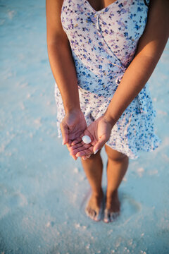 A white woman holding a shell on a sandy beach in a beach