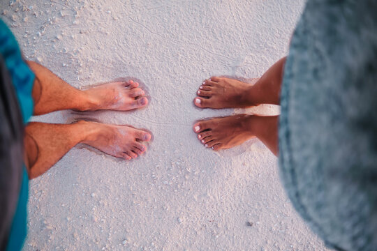 A couple standing barefoot on a sandy beach in a beach