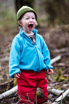 Elementary boy wearing blue jacket shouting while standing in forest
