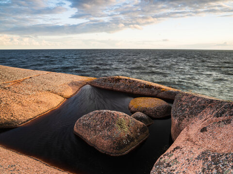 Tide pool formed in natural depression within flat granite shelf near sea