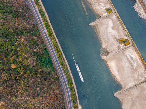 Overhead view of the Rhine River during low water, with a barge passing between a forested road and sandy sandbanks.