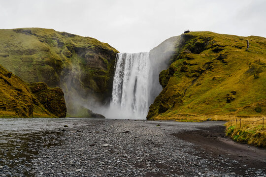 A powerful waterfall flows down mossy cliffs into a rocky riverbed