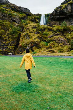 A white woman walks through grassy field toward a waterfall
