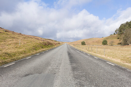 Long empty road amidst sandy landscape under cloudy sky