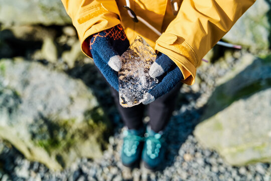 White Person holding a chunk of ice outdoors on rocky ground