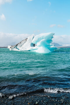 A large iceberg floats in icy water near a rocky shore