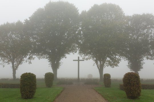 Gravel pathway leading towards tall cross near trees in foggy atmosphere