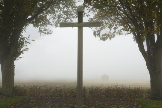 Tall religious cross between trees at foggy location