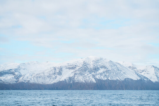 Snow-covered mountain range overlooks calm ocean water