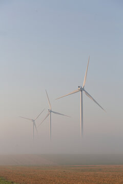 Fog around wind generators on landscape against clear sky