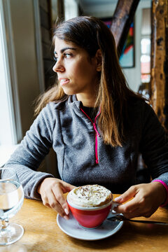 A white woman enjoys a cappuccino inside a cozy cafe