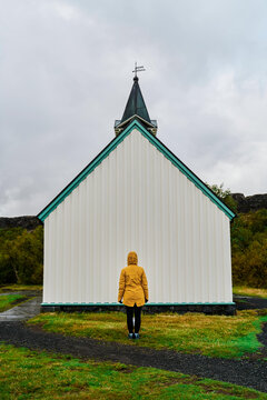 A person in a yellow jacket faces a small white church with steeple
