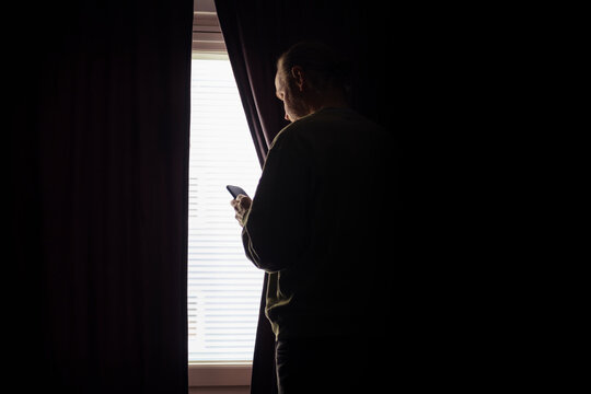 Senior man using smartphone while standing by window at home