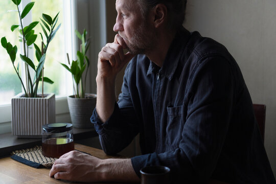 Thoughtful senior man with hand on chin looking through window at home