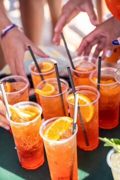 Hands reach for chilled orange cocktails during a sunny summer gathering with friends. Sparkling citrus drinks create a colorful social scene of sharing, celebration and seaside leisure.