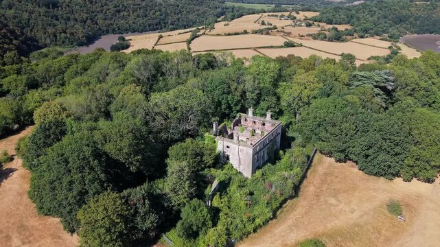 Abandoned ruins of Piercefield House surrounded by woodland near Chepstow, Wales, with open fields and the River Wye valley landscape stretching into the background