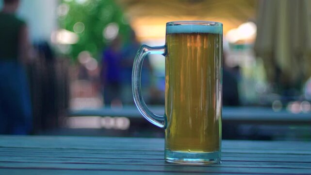 Tall glass mug of cold beer on outdoor restaurant table capturing refreshment, leisure and relaxed social dining atmosphere during daytime