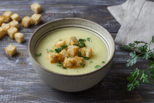 Creamy zucchini soup topped with golden croutons, fresh parsley and black pepper, served in a ceramic bowl on a dark rustic wooden table