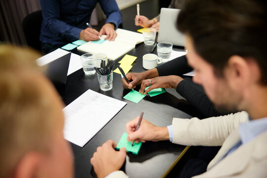 High angle view of business professionals writing ideas on adhesive notes in brainstorming session