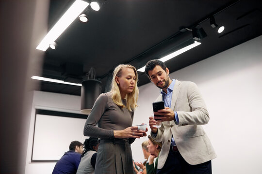 Low angle view of businessman sharing smart phone with colleague in break time
