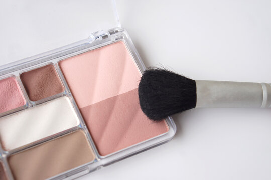 Close-up of a pink and neutral makeup palette with a soft blush brush on a clean white background, showcasing beauty cosmetics, makeup application, and feminine color tones.