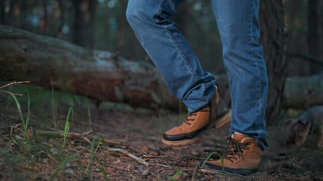 Man hiking in forest with boots stepping gently on moss-covered path. Fallen trees around as forest shadows move. Boots and nature dominate trail. Forest walking becomes immersive travel scene.