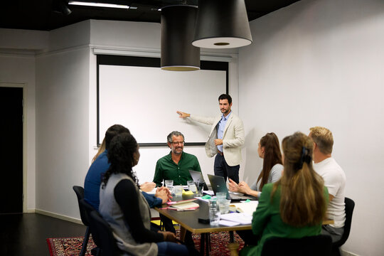 Businessman gesturing towards projection screen while talking his teammates