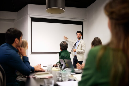 Businessman pointing at projection screen while talking to his coworkers in meeting room