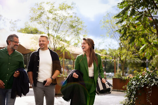 Happy businesswoman laughing while walking with male coworkers in office park