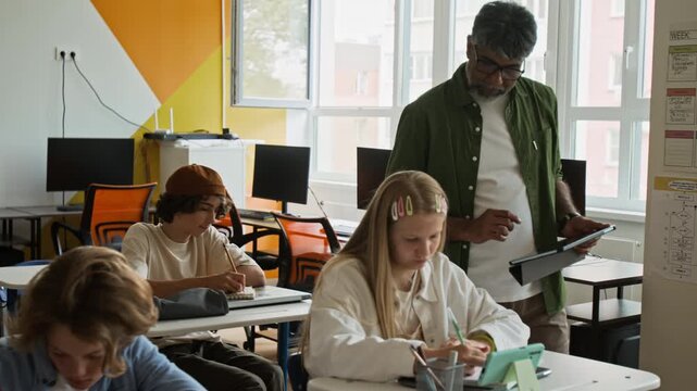 Middle aged teacher using tablet while helping Caucasian teenage girl in classroom, panning shot. Ideal for school promotional videos and e-learning advertisements